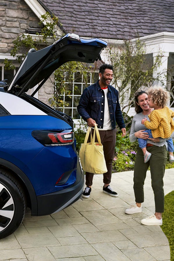 A young family loads a bag into the cargo area of an ID.4, shown in Dusk Blue Metallic parked in a residential home’s driveway.